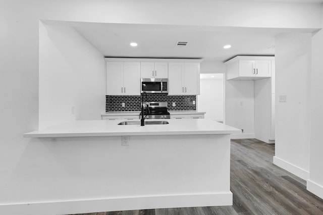 kitchen with dark wood-type flooring, sink, kitchen peninsula, appliances with stainless steel finishes, and white cabinetry