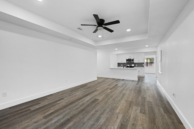 unfurnished living room with a raised ceiling, ceiling fan, and dark hardwood / wood-style floors