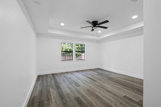 empty room with a raised ceiling, ceiling fan, and dark wood-type flooring