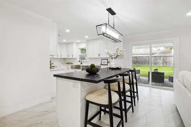 kitchen with white cabinetry, a center island, hanging light fixtures, a kitchen bar, and ornamental molding