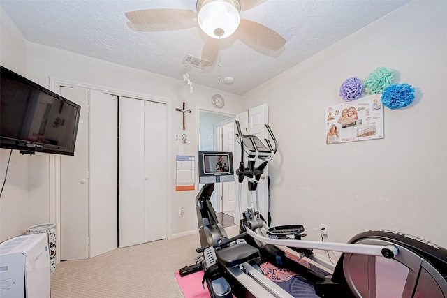 workout room with a textured ceiling, ceiling fan, and light carpet