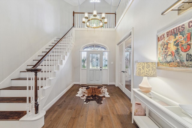 entrance foyer with hardwood / wood-style floors, a towering ceiling, french doors, and a notable chandelier