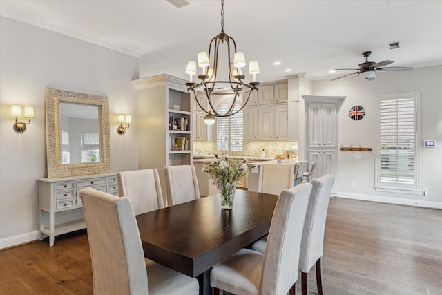 dining space featuring wood-type flooring, ceiling fan with notable chandelier, and ornamental molding