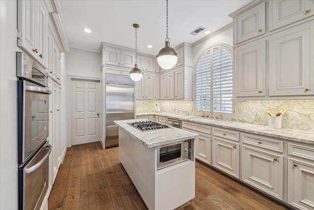 kitchen with sink, built in appliances, decorative backsplash, ornamental molding, and a kitchen island