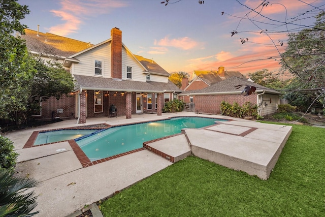 pool at dusk with an in ground hot tub, a yard, and a patio area