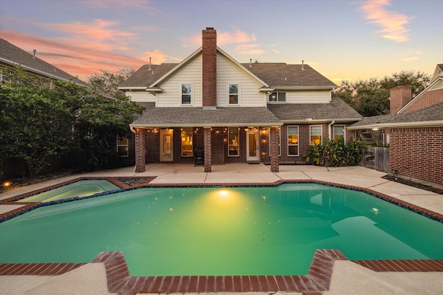 pool at dusk with an in ground hot tub and a patio