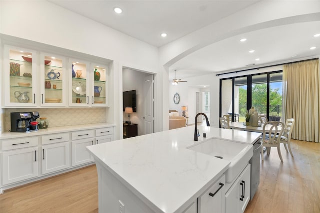 kitchen featuring light stone countertops, tasteful backsplash, ceiling fan, a center island with sink, and white cabinetry