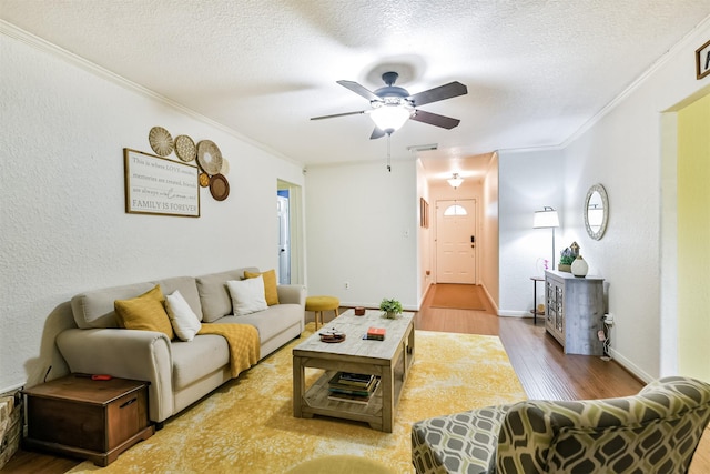 living room featuring a textured ceiling, light wood-type flooring, ceiling fan, and crown molding