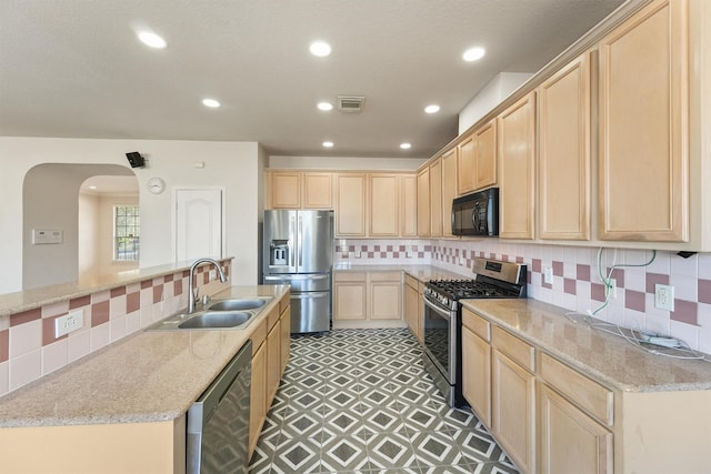 kitchen with light stone countertops, light brown cabinetry, stainless steel appliances, and sink