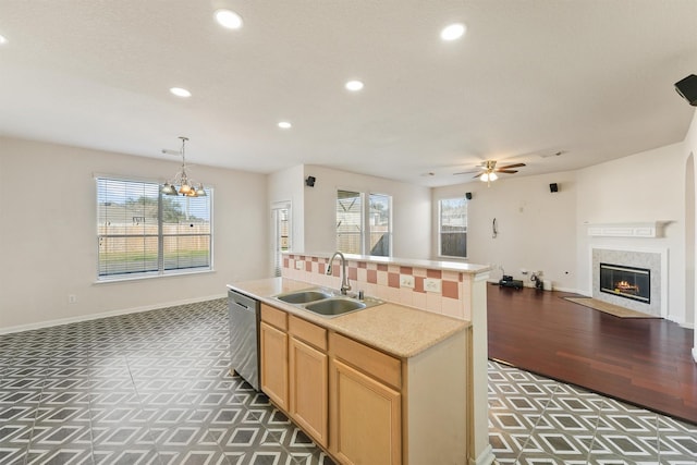 kitchen with a center island with sink, sink, hanging light fixtures, stainless steel dishwasher, and a fireplace