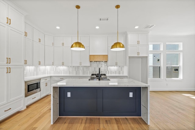 kitchen with hanging light fixtures, light stone countertops, an island with sink, white cabinetry, and stainless steel appliances