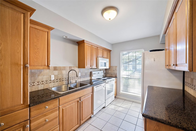 kitchen featuring tasteful backsplash, dark stone counters, white appliances, sink, and light tile patterned flooring