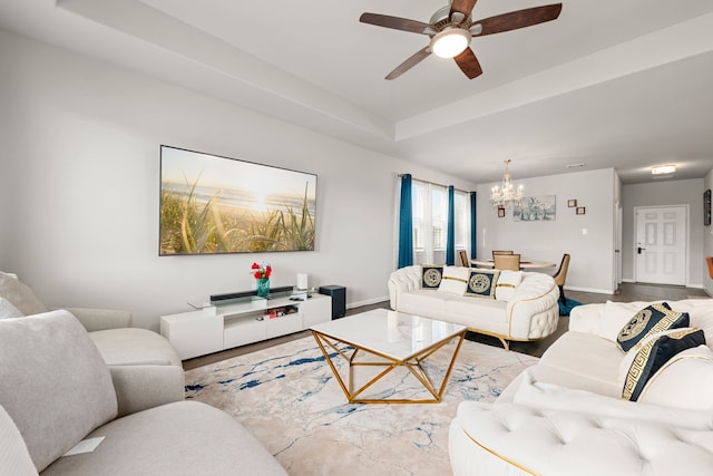 living room featuring a raised ceiling and ceiling fan with notable chandelier