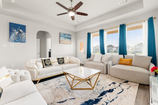 living room featuring ceiling fan, wood-type flooring, and a tray ceiling