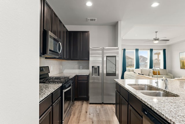 kitchen with ceiling fan, appliances with stainless steel finishes, light stone countertops, light hardwood / wood-style flooring, and sink