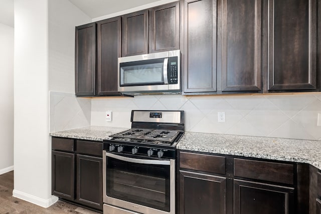 kitchen with dark wood-type flooring, appliances with stainless steel finishes, dark brown cabinetry, and light stone countertops