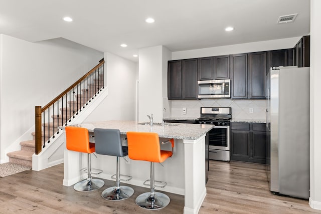 kitchen featuring a center island with sink, appliances with stainless steel finishes, light stone counters, a breakfast bar, and sink