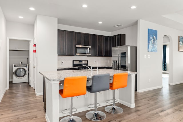 kitchen with a center island with sink, washer / clothes dryer, light stone countertops, a kitchen breakfast bar, and stainless steel appliances