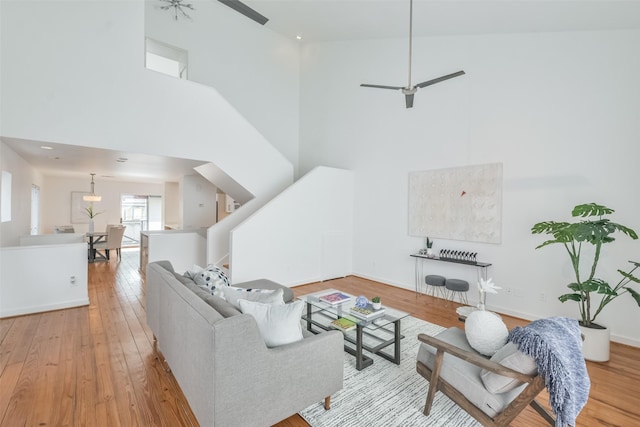 living room featuring a high ceiling, light wood-type flooring, and ceiling fan