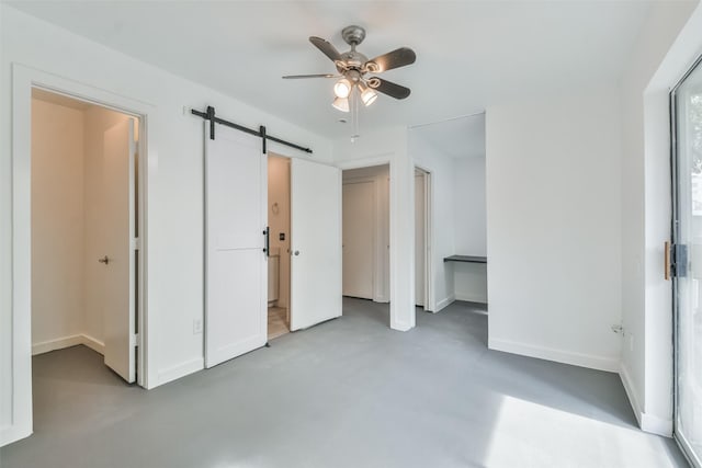 unfurnished bedroom featuring concrete flooring, a barn door, ceiling fan, and connected bathroom