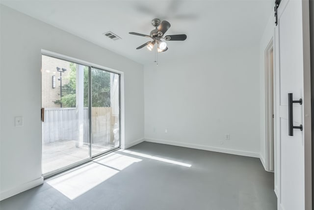 spare room with a barn door, concrete floors, and ceiling fan