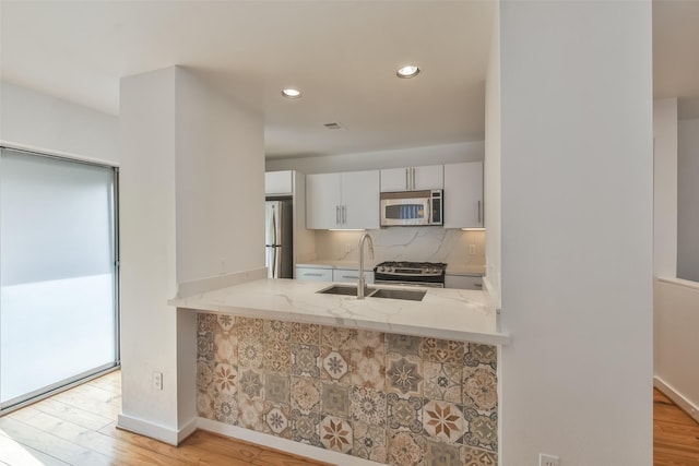 kitchen with light wood-type flooring, backsplash, light stone counters, stainless steel appliances, and white cabinetry