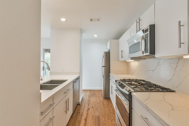 kitchen featuring sink, light stone countertops, light hardwood / wood-style floors, white cabinetry, and stainless steel appliances