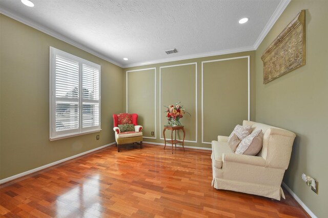 living area with wood-type flooring, a textured ceiling, and ornamental molding