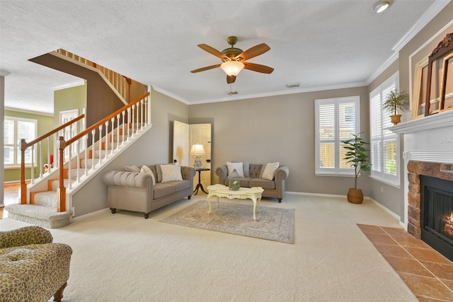 living room featuring ceiling fan, a stone fireplace, crown molding, carpet floors, and a textured ceiling