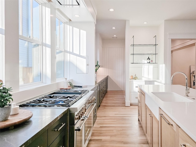 kitchen featuring high end range, sink, light hardwood / wood-style floors, and light brown cabinets