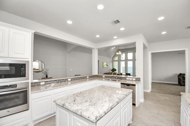 kitchen with kitchen peninsula, appliances with stainless steel finishes, sink, white cabinets, and a kitchen island