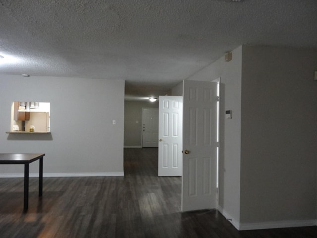 hallway featuring dark wood finished floors, baseboards, and a textured ceiling