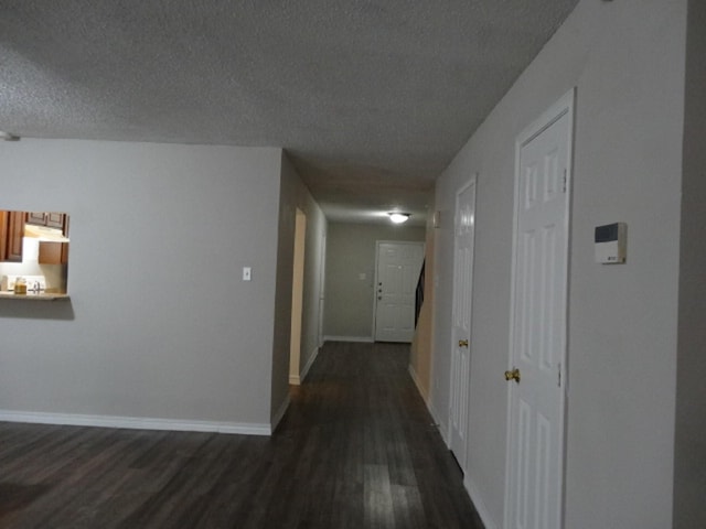 hall featuring dark wood-style flooring, baseboards, and a textured ceiling