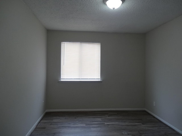 empty room with a textured ceiling, baseboards, and wood finished floors