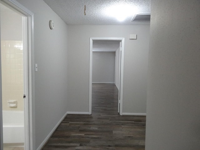 corridor featuring baseboards, a textured ceiling, visible vents, and wood finished floors