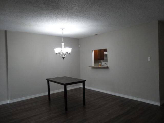 unfurnished dining area with dark wood-type flooring, a textured ceiling, baseboards, and an inviting chandelier