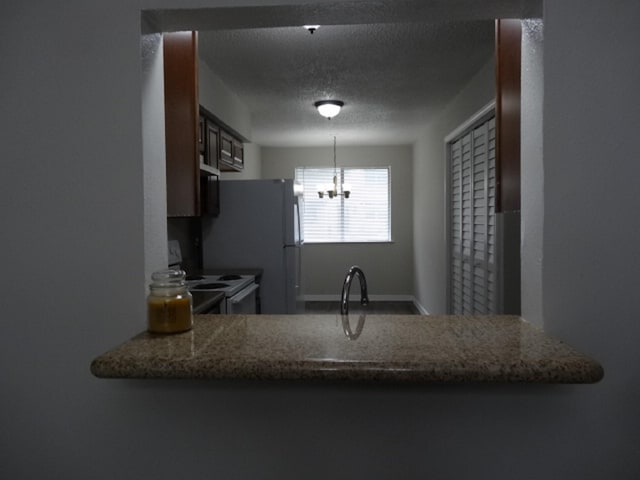kitchen with a chandelier, a peninsula, a textured ceiling, baseboards, and electric range