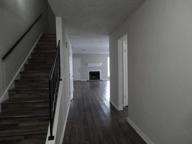 hallway with dark wood-style floors, baseboards, and stairs