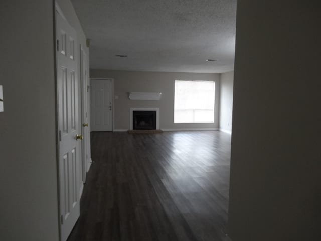 unfurnished living room with a fireplace with raised hearth, dark wood-style floors, baseboards, and a textured ceiling