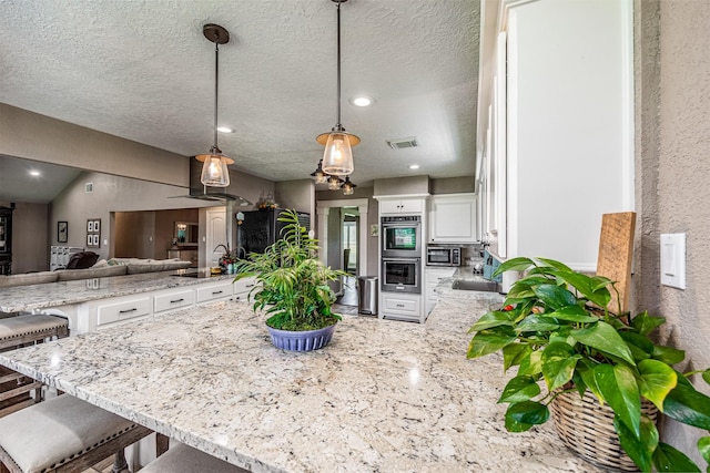 kitchen with a breakfast bar, white cabinets, hanging light fixtures, and a textured ceiling