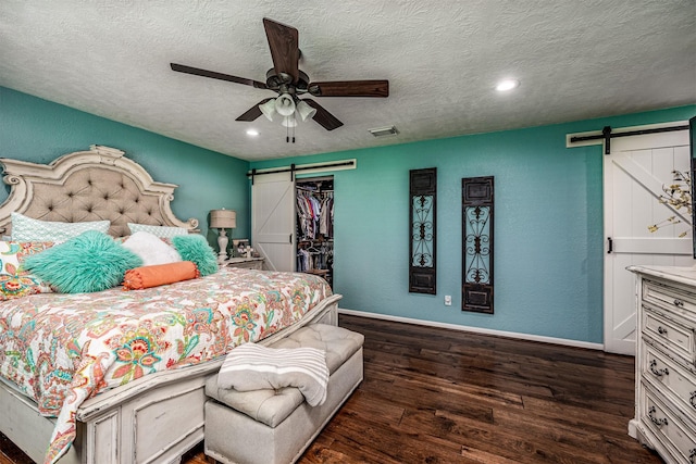 bedroom with ceiling fan, a barn door, dark wood-type flooring, and a closet