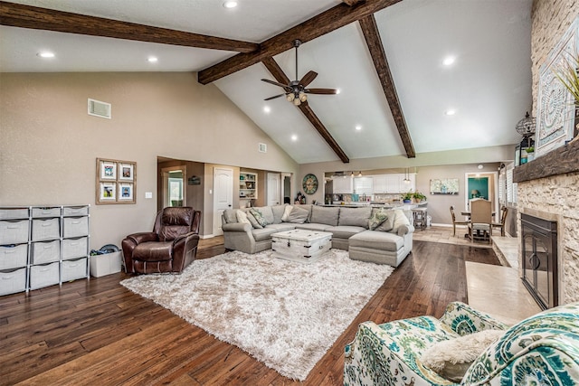 living room featuring ceiling fan, dark wood-type flooring, a stone fireplace, beamed ceiling, and high vaulted ceiling