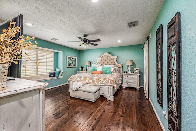 bedroom featuring a barn door, ceiling fan, dark hardwood / wood-style flooring, and a textured ceiling