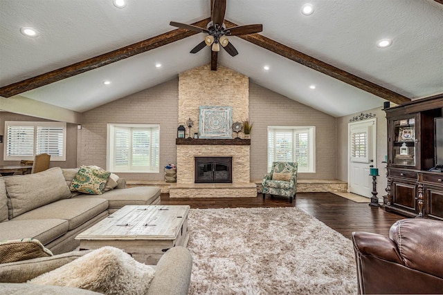 living room featuring lofted ceiling with beams, a stone fireplace, ceiling fan, dark hardwood / wood-style flooring, and brick wall