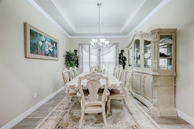 dining space with an inviting chandelier, a raised ceiling, light hardwood / wood-style floors, and crown molding