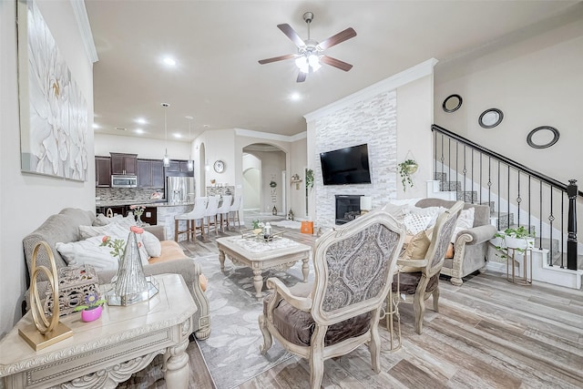 living room featuring ceiling fan, light hardwood / wood-style floors, a stone fireplace, and ornamental molding