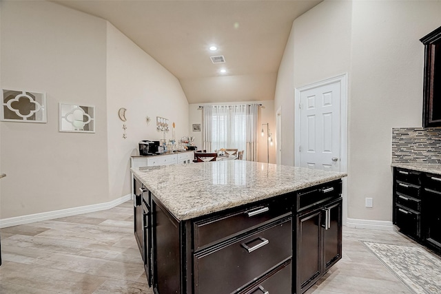 kitchen featuring backsplash, light stone counters, a center island, and vaulted ceiling