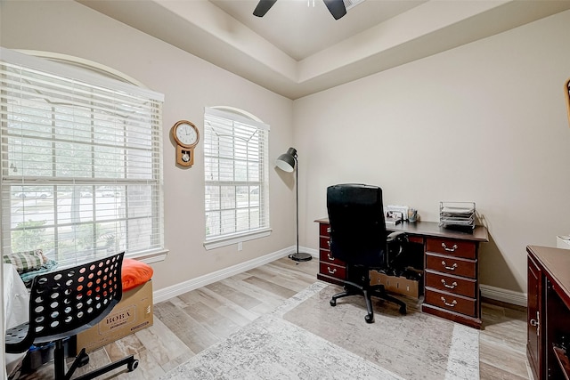 office space featuring a ceiling fan, a tray ceiling, light wood-style flooring, and baseboards