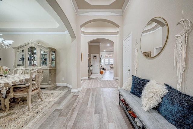 foyer featuring arched walkways, ornamental molding, light wood-style flooring, and baseboards