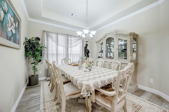 dining room featuring visible vents, baseboards, light wood finished floors, a raised ceiling, and an inviting chandelier